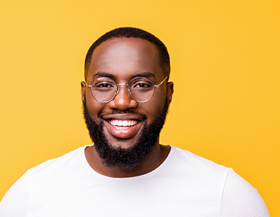 Un homme noir avec des lunettes et une barbe souriant sur fond jaune.